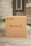 A cardboard box labeled 'MEALPRO' with the tagline 'EAT WITH PURPOSE' is placed outside a house. The box has a label indicating it contains perishable items and should be handled with care. There is grass visible to the left side and a brick wall partially visible on the right. The house door and part of a window can be seen in the background.