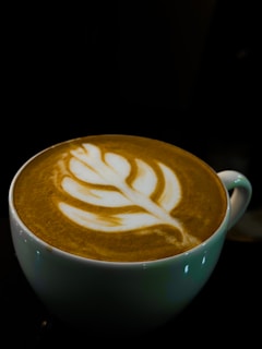 Close-up of a custom latte with delicate leaf art in a white cup against a dark olive green background