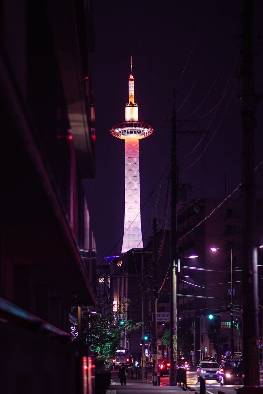 a city street at night with a tall tower in the background