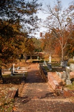 a brick path leading to a cemetery with a clock tower in the background