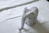 A towel is creatively folded into the shape of an elephant and placed on a neatly made bed with white sheets.