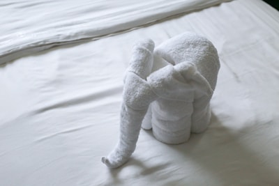 A towel is creatively folded into the shape of an elephant and placed on a neatly made bed with white sheets.