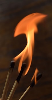 Three lit matches with their flames prominently visible, set against a dark background. The flames vary in size and shape, creating a dynamic and energetic display.