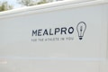 The side of a white vehicle displays the meal service logo 'MEALPRO' with the tagline 'For the Athlete in You'. Next to the text is a graphic combining a lightbulb and a fork.