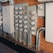 A row of multiple electrical meters and panels is mounted on a brick wall. The setup includes several round meters with clear covers, metal conduits, and electrical boxes. The equipment is organized and securely installed.