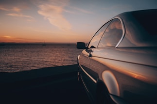 A sleek luxury car parked by the coast at sunset, reflecting the warm colors of the sky