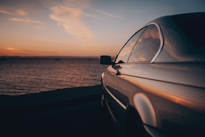 A shiny sedan reflecting the golden hues of a Huatulco sunset near the shore.