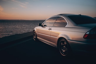 A sleek luxury car parked on a scenic coastal road at sunset.