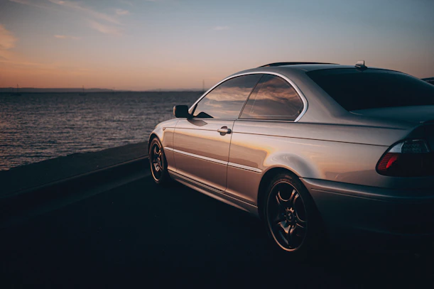 A sleek silver Mercedes-Benz gliding along a coastal road at sunset, reflecting soft periwinkle hues.