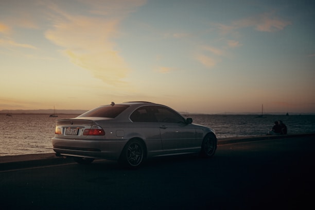 A sleek vintage car parked by the sea at sunset, highlighting timeless elegance.
