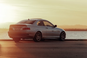 A luxury sedan parked beside a serene lake during golden hour