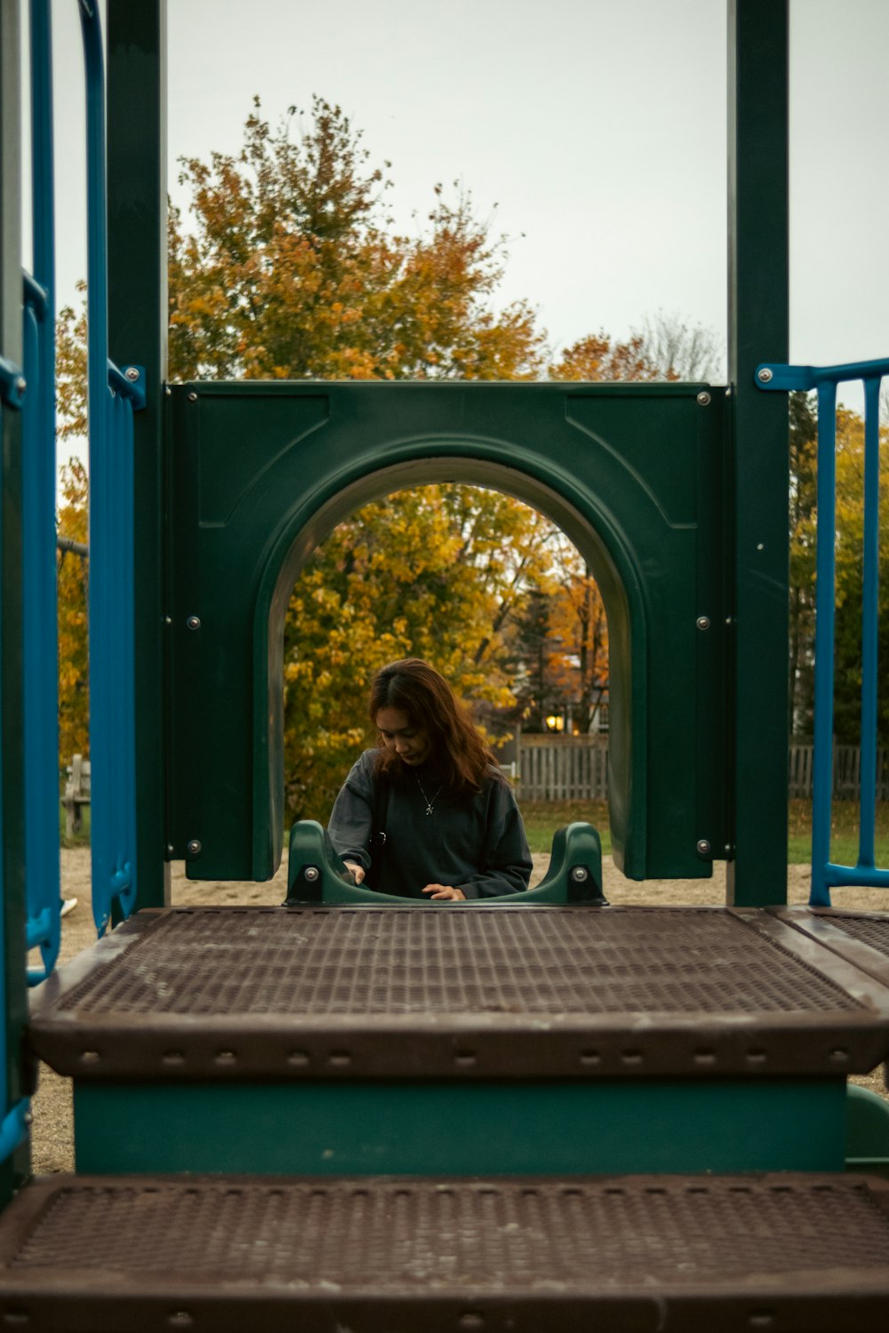 a woman sitting on a green and blue playground