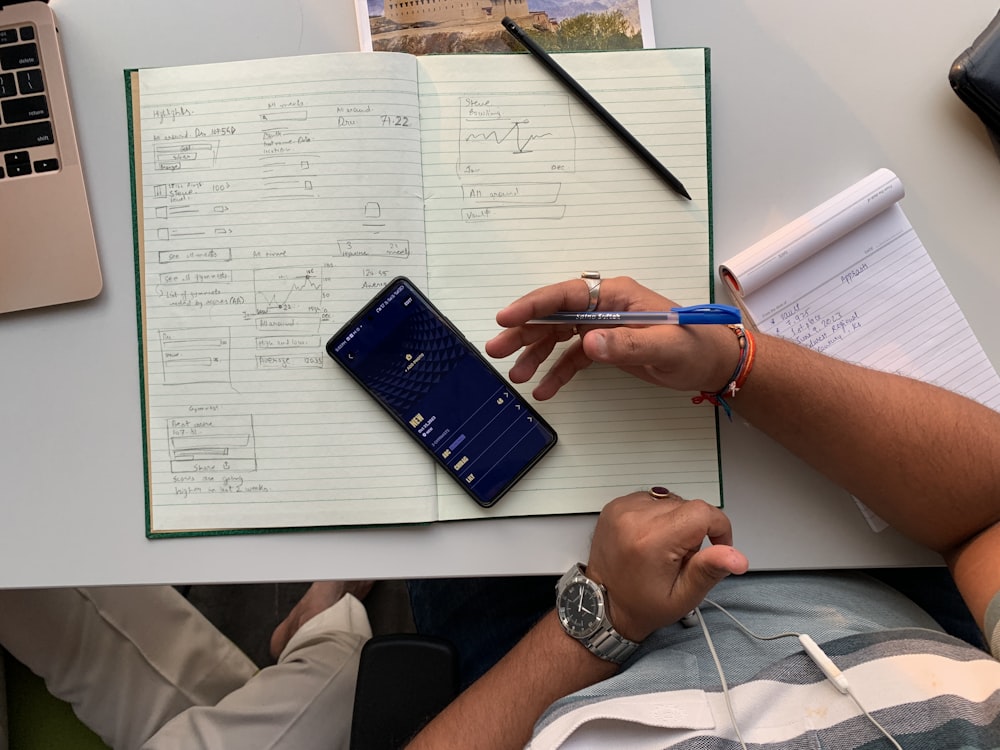 a person sitting at a desk with a notebook and a cell phone