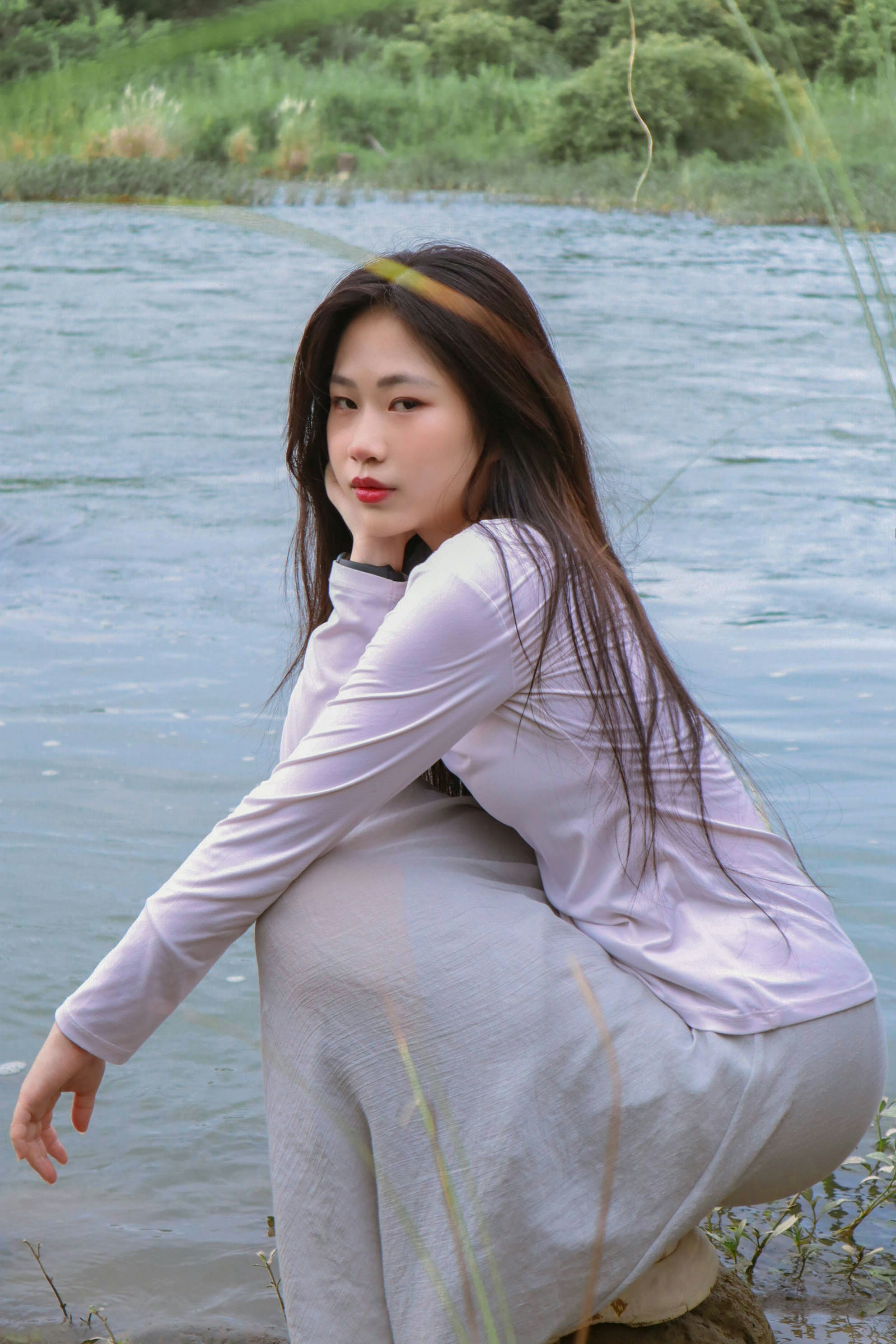 A woman sitting on a rock next to a body of water photo – Free Portrait ...