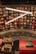A bookstore filled with a variety of books on wooden shelves arranged in a circular pattern. Bright, white overhead lights create a modern ambiance. Decorative elements such as wrapped gifts are placed on a red, ornately designed ledge.