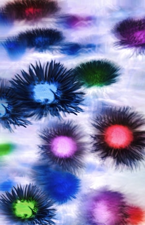 Various colorful, abstract floral designs appear to float against a soft, blurred background. Each design resembles a flower with a central core and radiating petals in vibrantly contrasting colors.