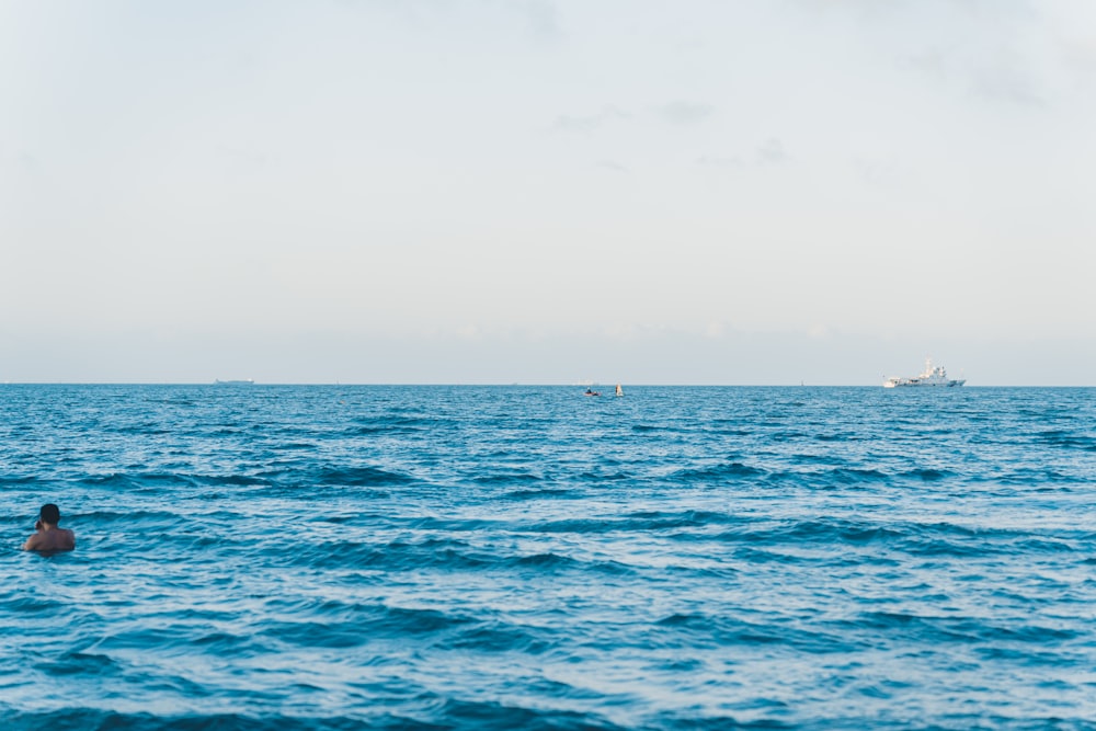 a person swimming in the ocean with a boat in the distance