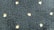 A textured dark fabric with a pattern of small, light-colored, star-like shapes evenly distributed across the surface. The texture appears plush and thick, indicating a potential use in upholstery or carpeting.