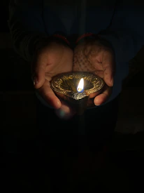 Hands holding a glowing diya lamp surrounded by lotus petals.