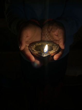 Hands gently holding rich, dark vermicompost beside a row of glowing handcrafted Panchagavya diyas.