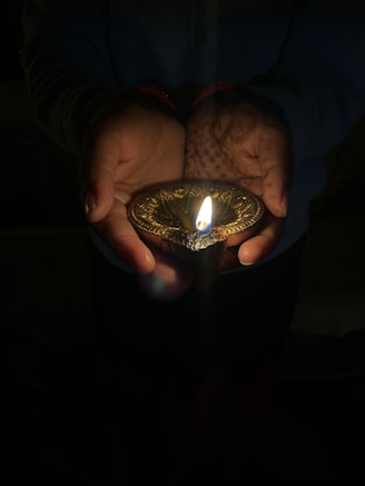 A warm, inviting image of hands offering a glowing diya lamp symbolizing seva and giving.