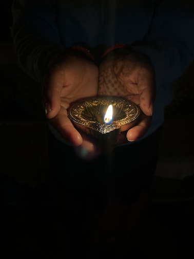 A warm, inviting image of hands offering a glowing diya lamp symbolizing seva and giving.