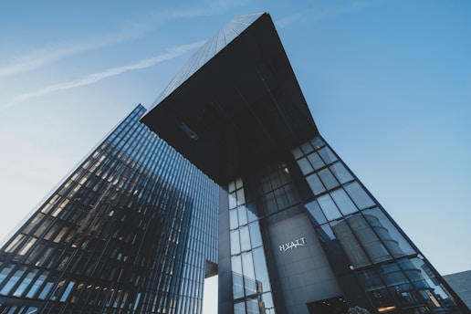 Tall, modern skyscrapers displaying sleek glass facades rise against a clear blue sky, creating an impressive urban landscape. One building prominently features the Hyatt logo.