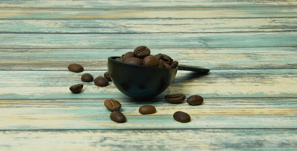 a black bowl filled with coffee beans on top of a wooden table