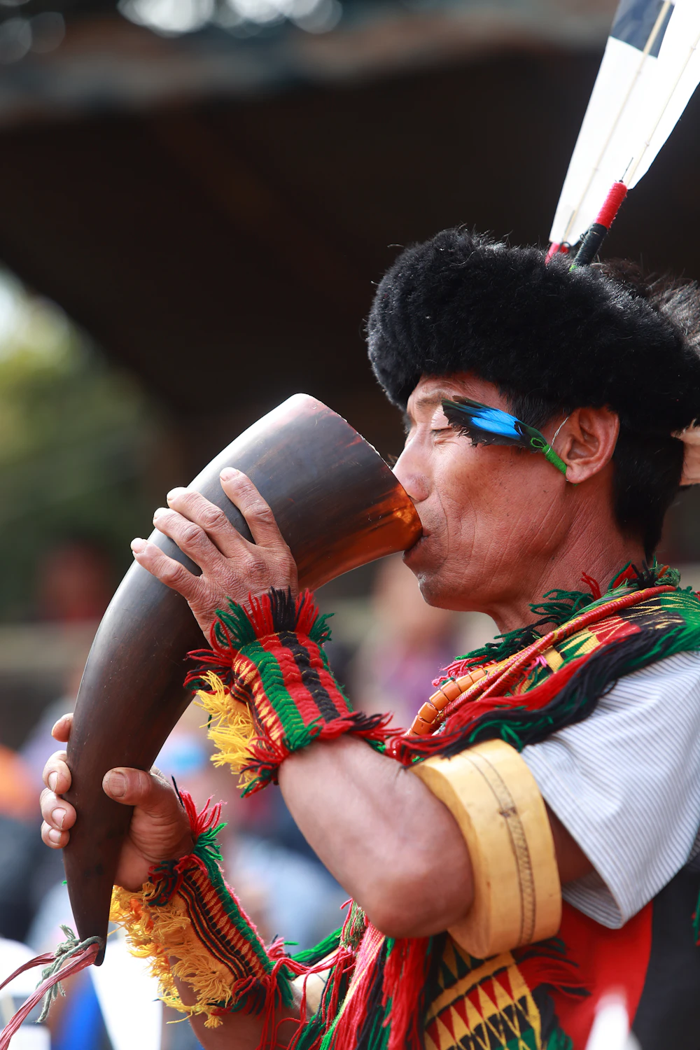 A Naga man in traditional dress blowing a horn