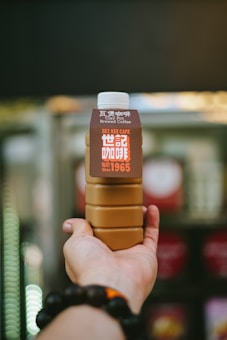 A hand holding a bottle of brewed coffee labeled with the words 'Clay Pot Brewed Coffee' and 'SEI KEE CAFE Since 1965'. The label has a brown and white color scheme with a distinctive design.