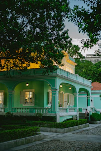 Charming colonial-style house with vibrant colors and lush tropical plants surrounding the entrance.