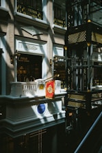 An indoor scene of a mall or shopping center featuring a luxury Ralph Lauren storefront with a Polo brand sign. The architectural design is ornate, with classical elements such as balconies, decorative light fixtures, and intricate moldings. Gold and black decorative motifs adorn the structure in the right side of the image.