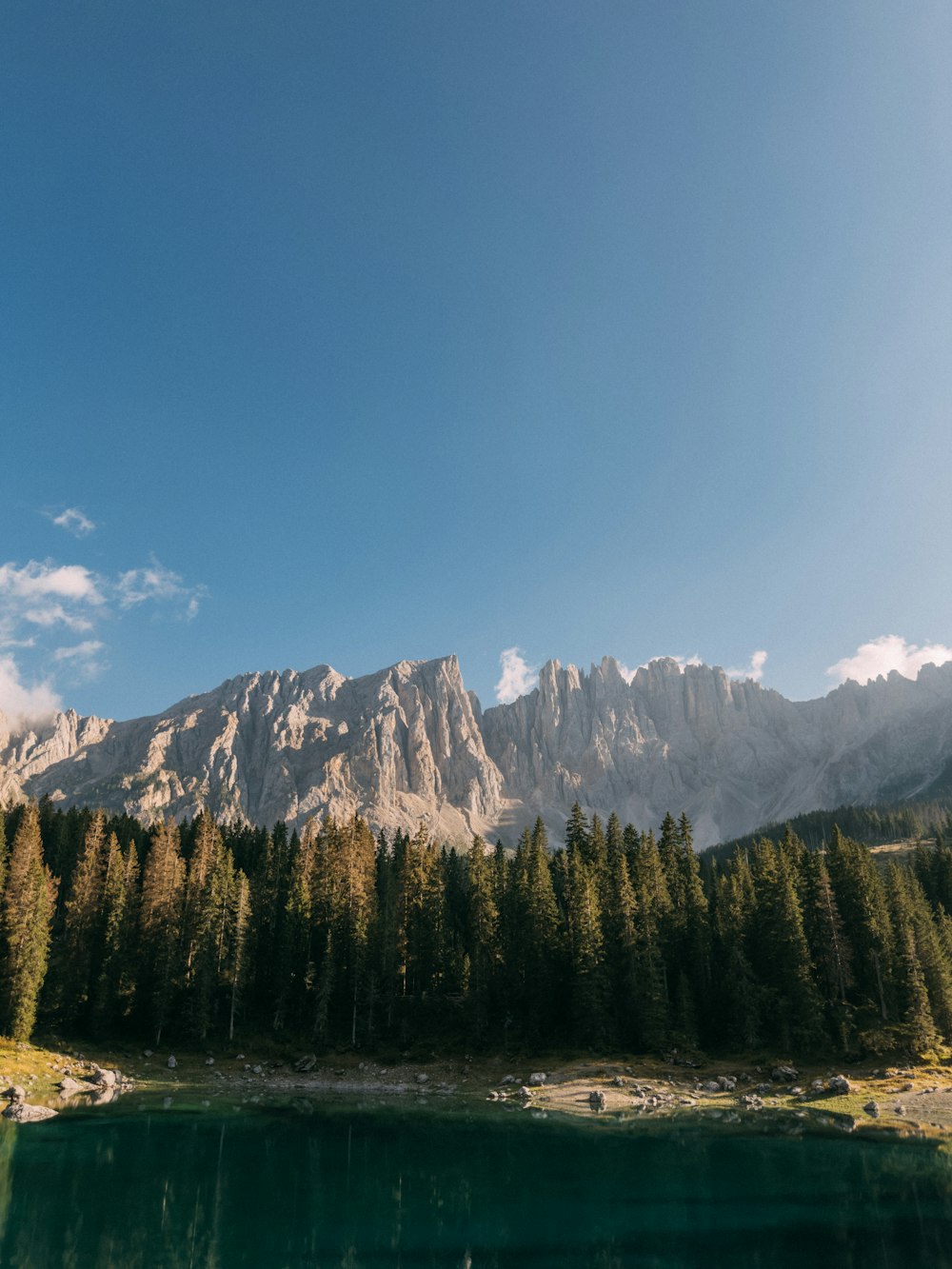 a lake surrounded by trees and mountains under a blue sky