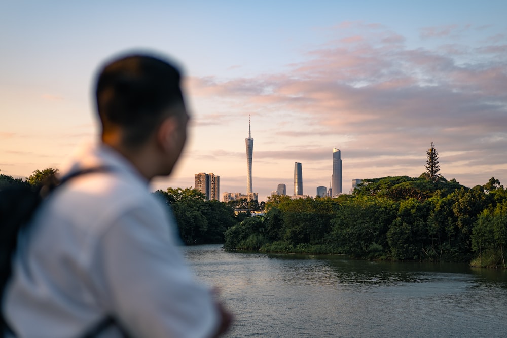 a man standing next to a river with a city in the background