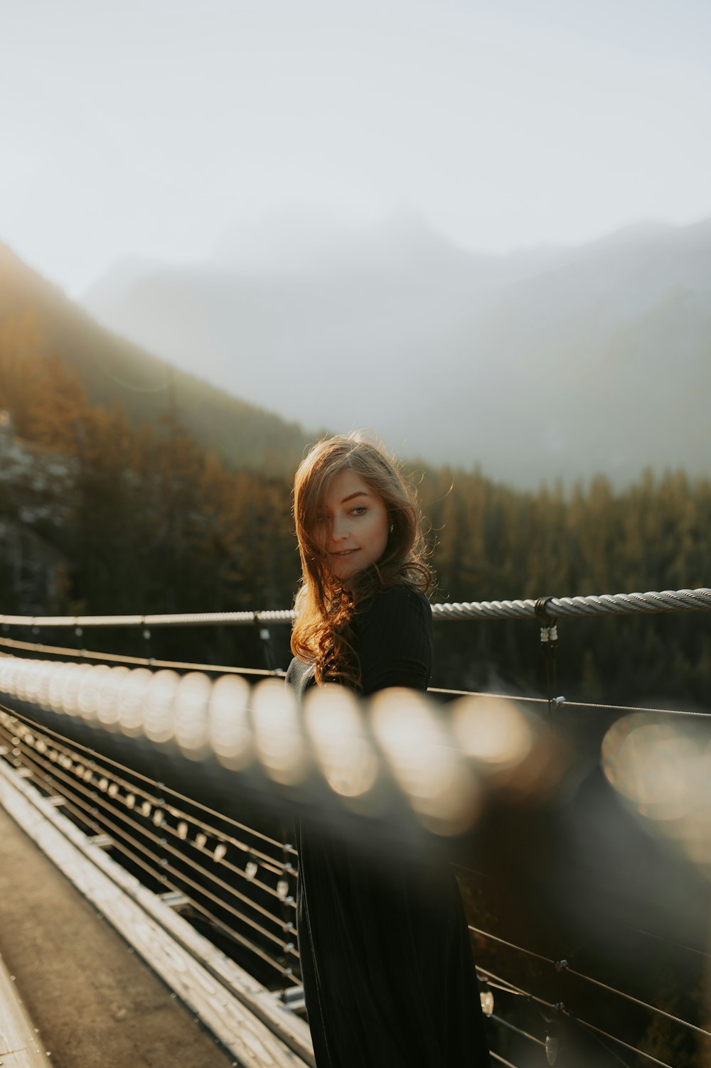 a woman standing on a bridge with mountains in the background