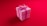 A pink gift box with a large pink ribbon and bow on top, set against a vibrant red background. The box has a yellow decorative center in the middle of the bow.