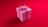 A pink gift box with a large pink ribbon and bow on top, set against a vibrant red background. The box has a yellow decorative center in the middle of the bow.
