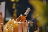 A bottle of white wine is nestled in a chilled container surrounded by bunches of green grapes. The setting is elegant, with soft lighting creating a warm and inviting atmosphere.