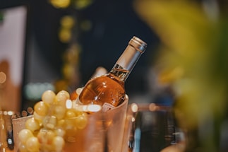 A bottle of white wine is nestled in a chilled container surrounded by bunches of green grapes. The setting is elegant, with soft lighting creating a warm and inviting atmosphere.