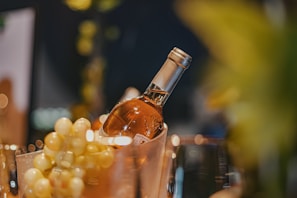 A chilled bottle of crisp white wine nestled in a bed of fresh grape leaves on a cream linen cloth.