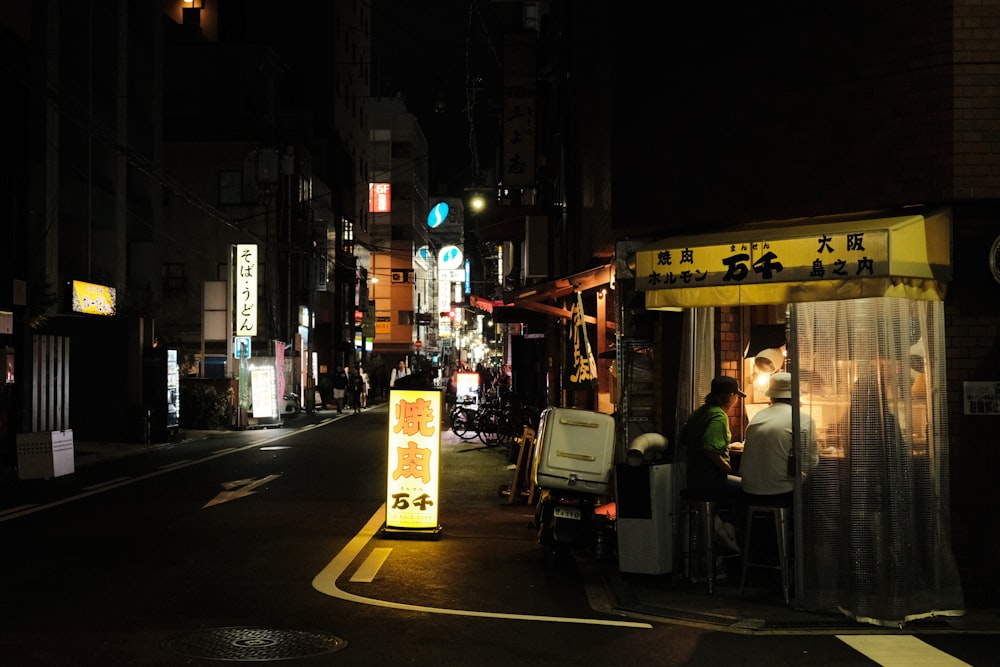 a city street at night with people sitting at tables