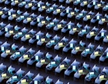 An array of identical office cubicles with computers on each desk, displaying various bright screens. The desks are lined up in a grid pattern, filling the entire space. Each workstation appears to be equipped with standard office items such as chairs, monitors, keyboards, and phones.