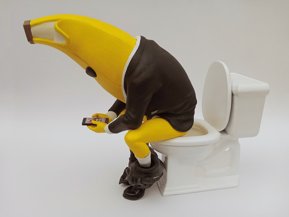 a toy banana sitting on top of a toilet