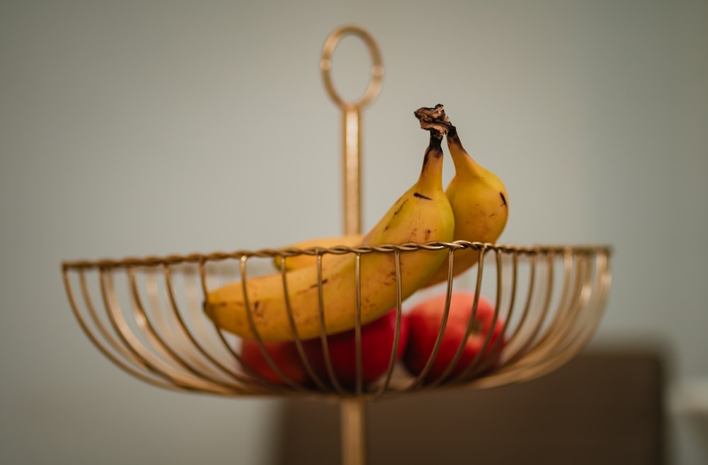 two bananas and three apples in a metal basket