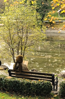 A person reading a tablet on a park bench, surrounded by autumn leaves.