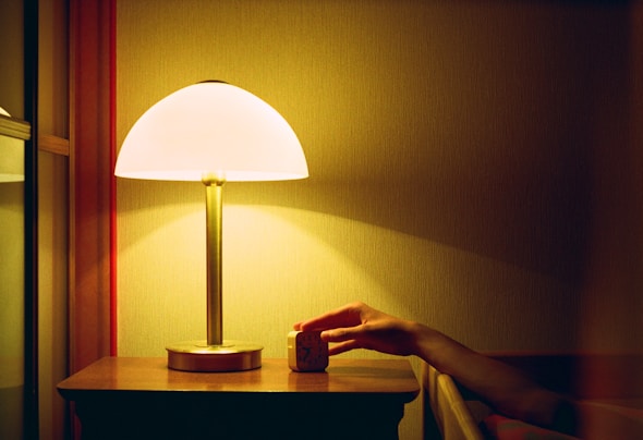 a person's hand on a table next to a lamp