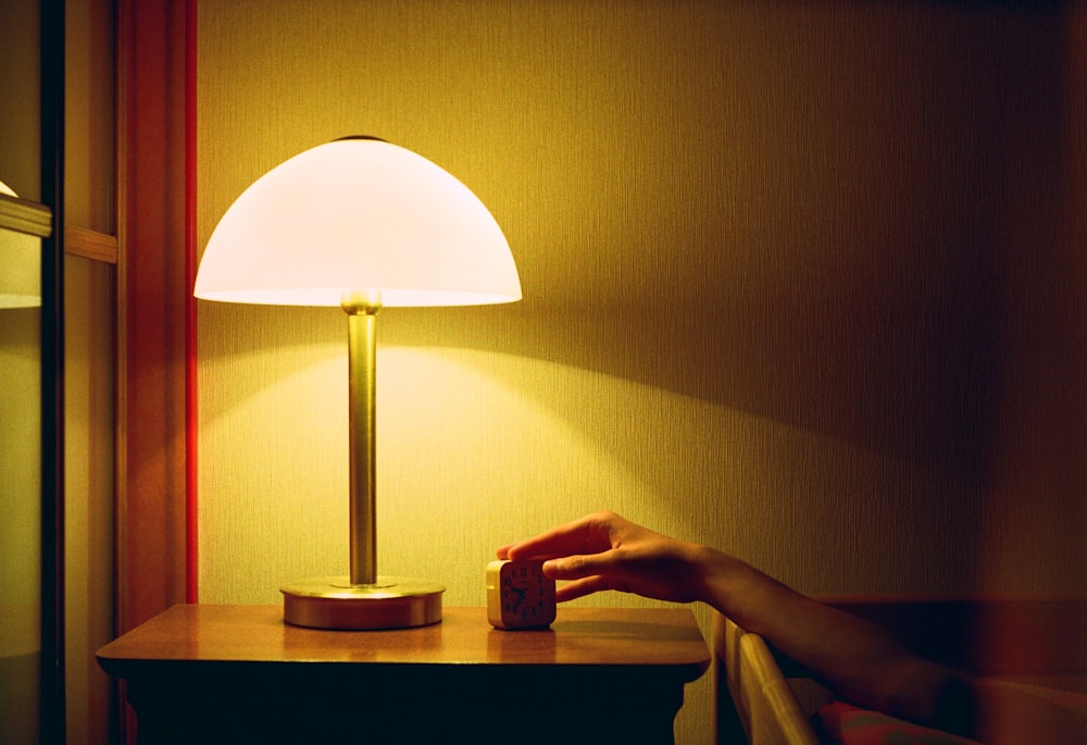 a person's hand on a table next to a lamp