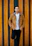 A stylish young man confidently wearing a minimalist brown jacket from Swag, standing against a cream-colored wall.