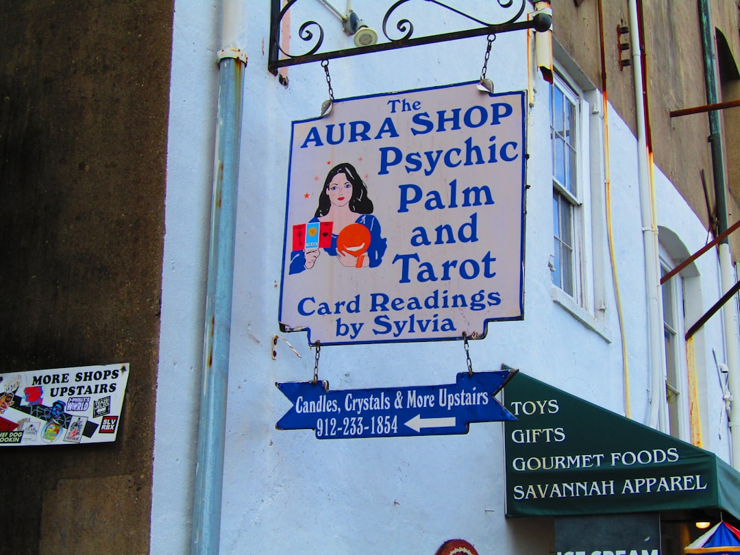 a sign on the side of a building that says aura shop psychic palm and tar, A rusty sign advertising a psychic and tarot 