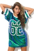 A person is wearing a sequined dress with the number 86 on the front. The dress is predominantly green and blue with sparkly sequins, and the person has long, wavy hair. They have an arm raised above their head and are wearing multiple bracelets.
